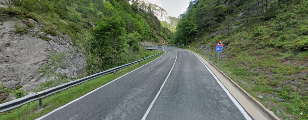 Curva de carretera de montaña en la ruta motera en Pirineos, señal de 50 km/h, asfalto entre rocas y bosque; tramo ideal para ruta motera transpirenaica.