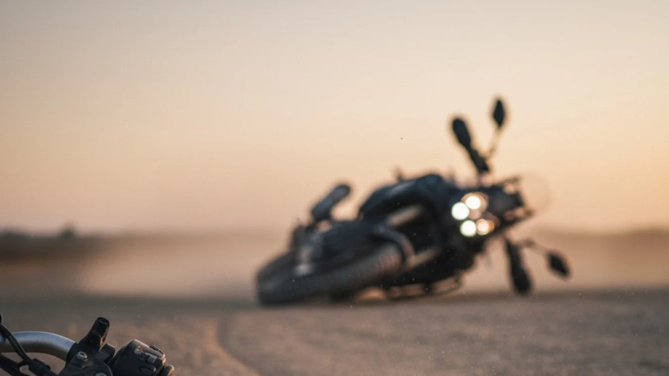 Arrastrón leve en grava; raspón en paramano y contrapeso con la moto negra desenfocada al fondo.