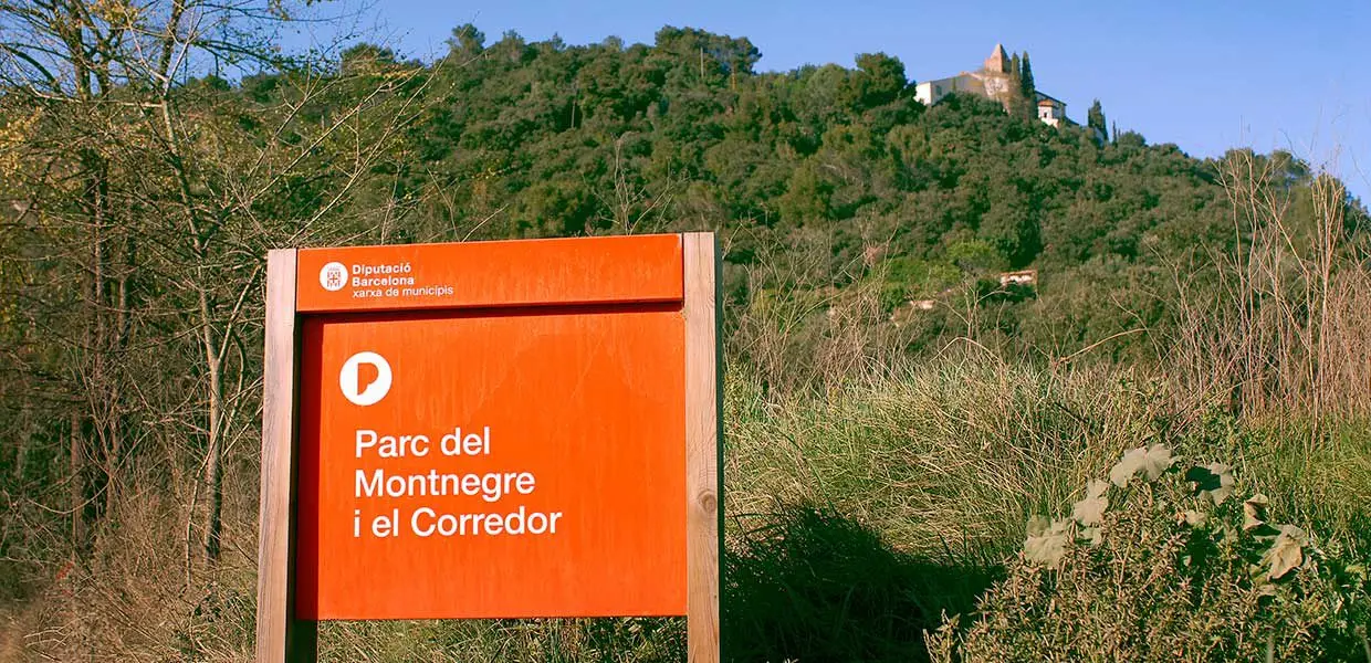 Cartel del Parc del Montnegre i el Corredor frente a una colina boscosa, cerca de Barcelona.